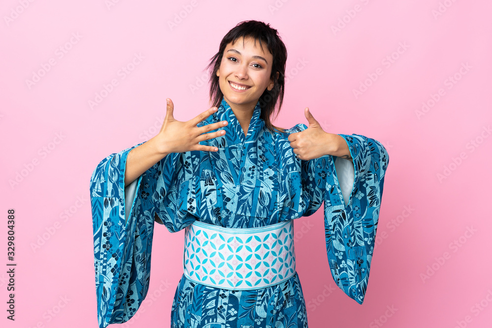 Young woman wearing kimono over isolated blue background counting six with fingers Young woman wearing kimono over isolated blue background counting six with fingers