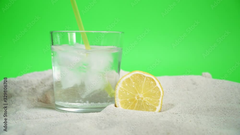 transparent glass with ice and sparkling water on the sand on a green background transparent glass with ice and sparkling water on the sand on a green background