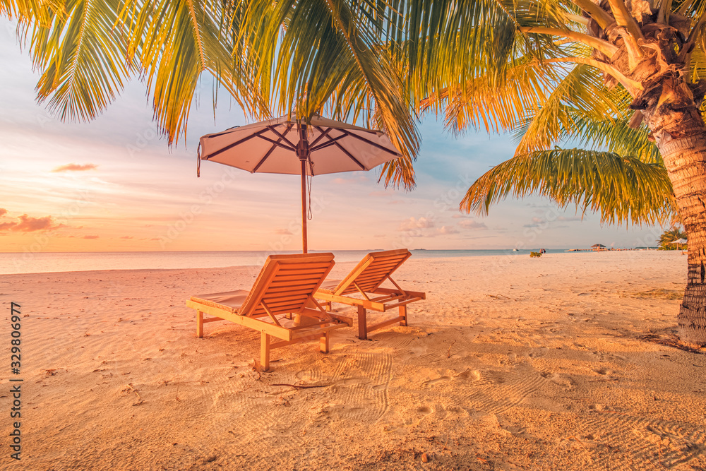 Obraz premium Beautiful tropical sunset scenery, two sun beds, loungers, umbrella under palm tree. White sand, sea view with horizon, colorful twilight sky, calmness and relaxation. Inspirational beach resort hotel