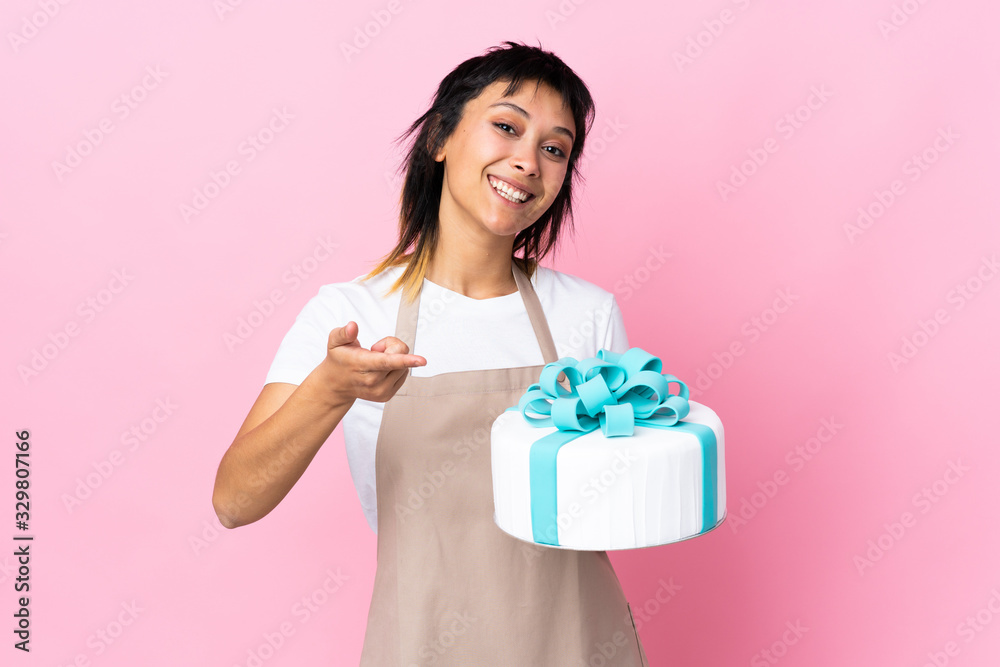 Uruguayan Pastry chef holding a big cake over isolated pink background points finger at you Uruguayan Pastry chef holding a big cake over isolated pink background points finger at you