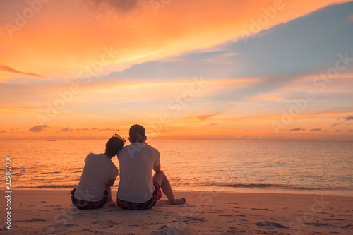 Couple in love watching sunset together on beach travel summer holidays. People silhouette from behind sitting enjoying view sunset sea on tropical destination vacation. Romantic couple on the beach © icemanphotos