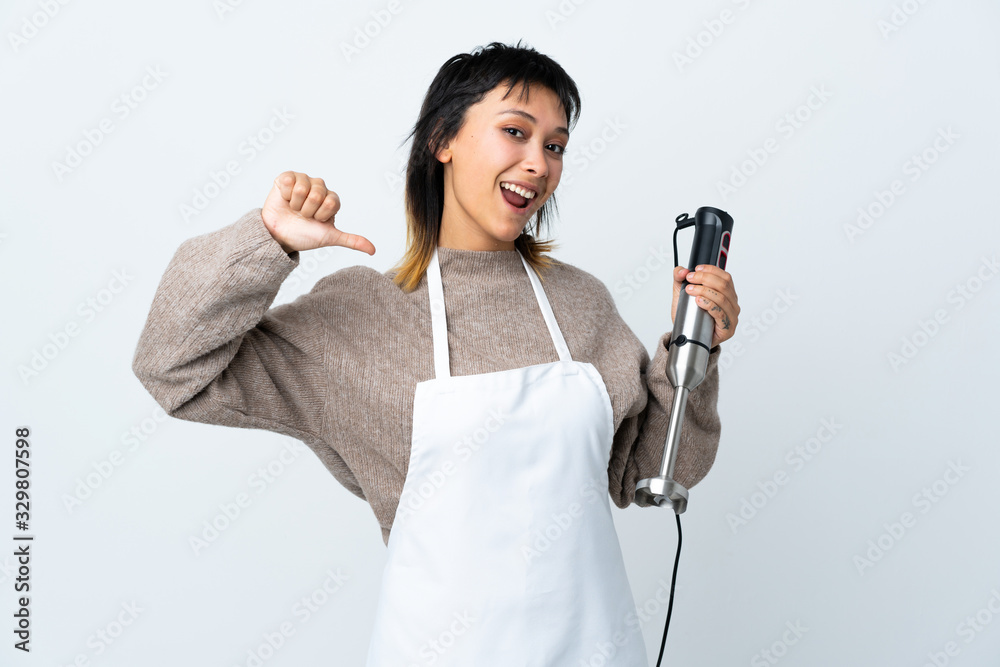 Chef Uruguayan girl using hand blender over isolated white background proud and self-satisfied