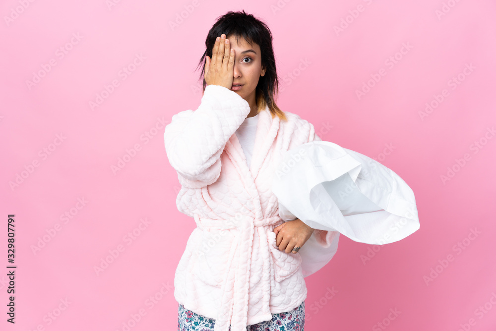 Young Uruguayan woman in pajamas over isolated pink background covering a eye by hand Young Uruguayan woman in pajamas over isolated pink background covering a eye by hand