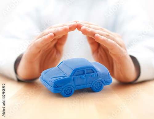 Car insurance concept with blue car toy covered by hands