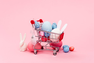 Colorful easter eggs and decorative bunnies in cart on pink background