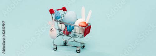 Colorful easter eggs and decorative rabbits in cart on blue, panoramic shot