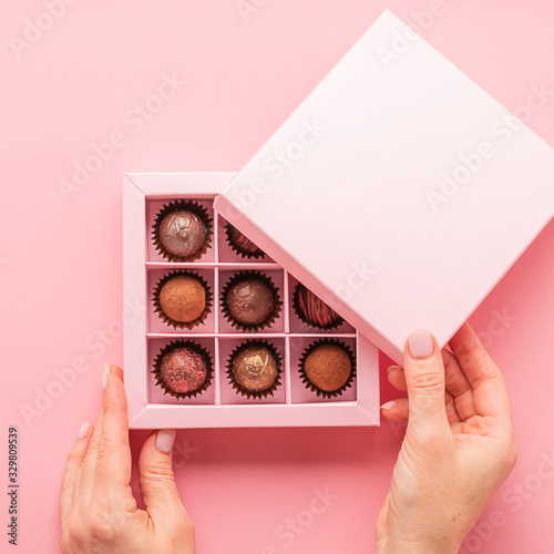 Female hand opens a box with sweets pink background . Gifts festive food love concept. Horizontal frame