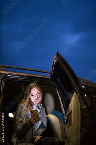 Young woman with her cell phone sitting in the backseat of a car, getting ready to travel (color toned image; shallow DOF) photo