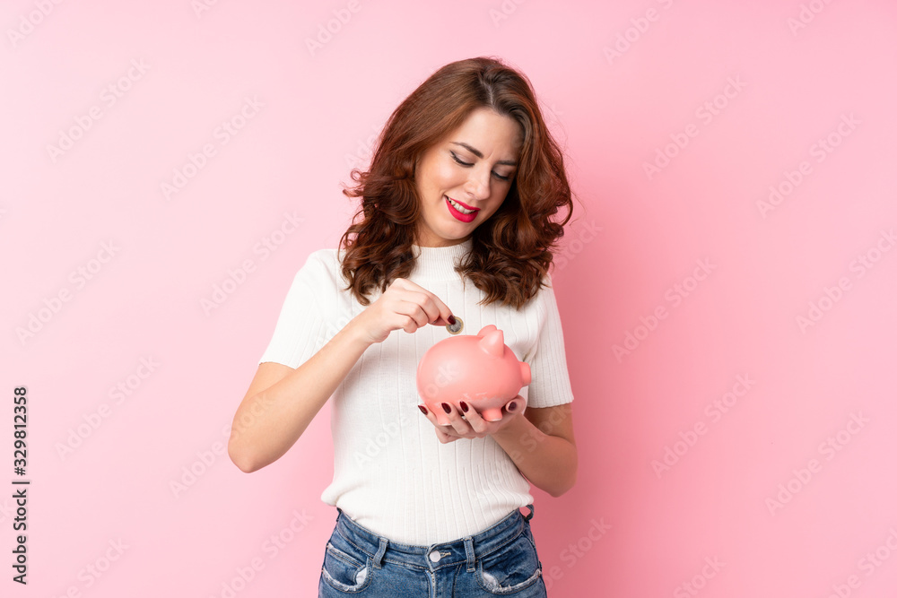 Young Russian woman over isolated pink background holding a big piggybank