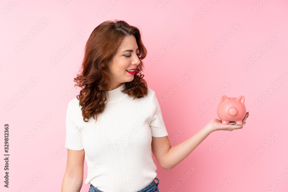 Young Russian woman over isolated pink background holding a big piggybank Young Russian woman over isolated pink background holding a big piggybank
