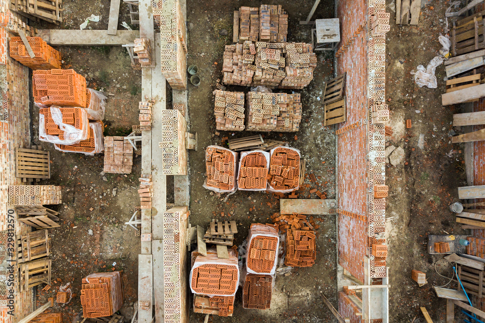 Aerial view of building site for future brick house, concrete foundation floor and stacks of yellow clay bricks for construction.