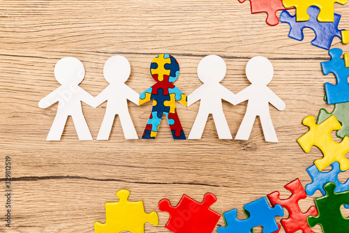 Top view of special kid with autism among another and pieces of multicolored puzzle on wooden background photo