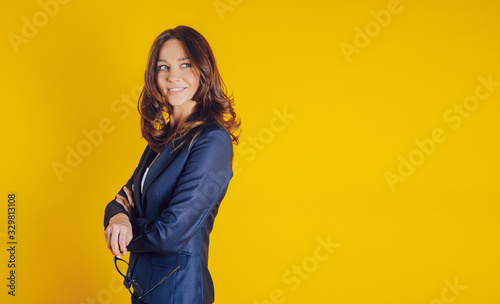 A beautiful young woman dressed elegantly as a teacher, like a bissnes lady, smiling and well placed on a yellow background © Kantemir Production
