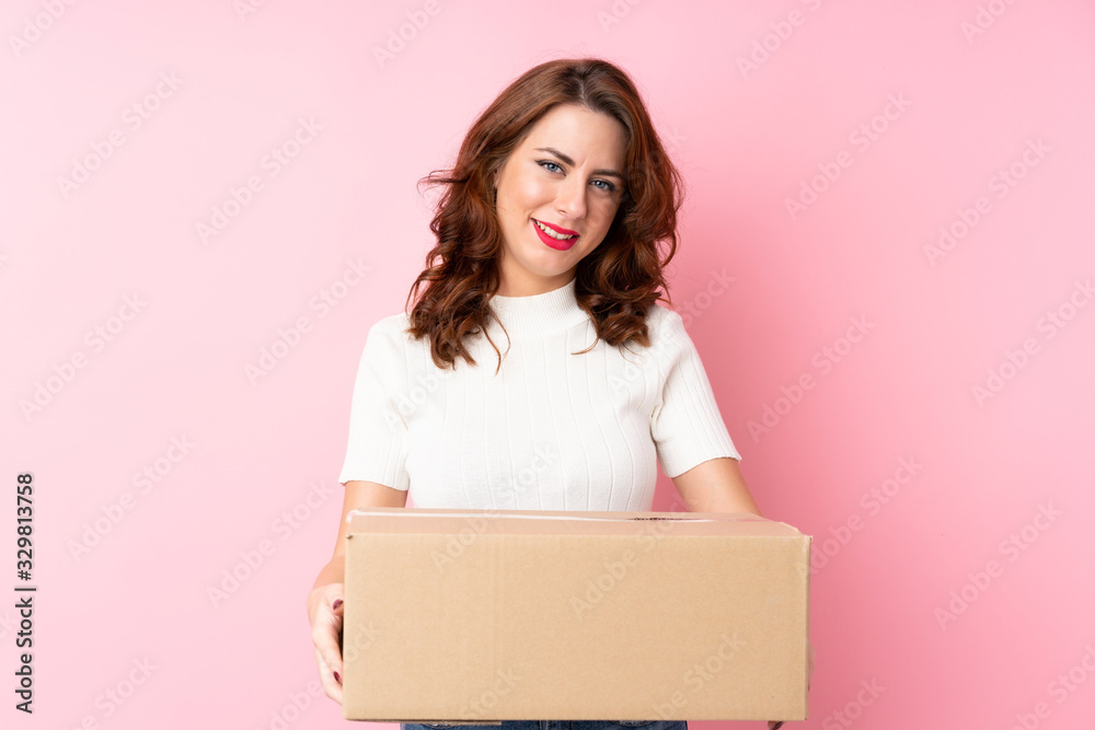Young Russian woman over isolated pink background holding a box to move it to another site Young Russian woman over isolated pink background holding a box to move it to another site