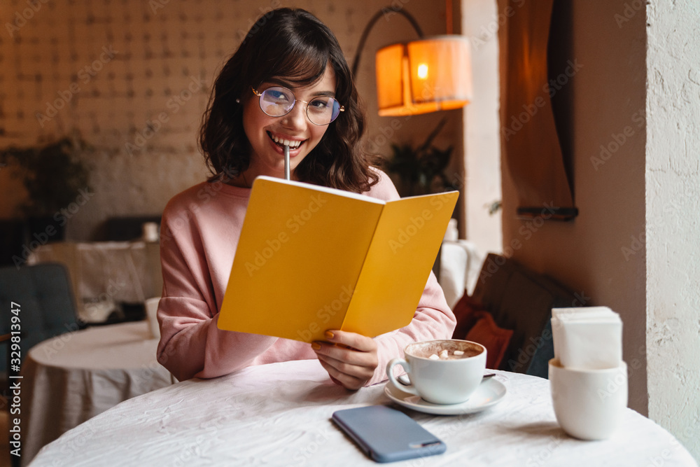 Brunette young woman indoors in cafe reading book. Brunette young woman indoors in cafe reading book.