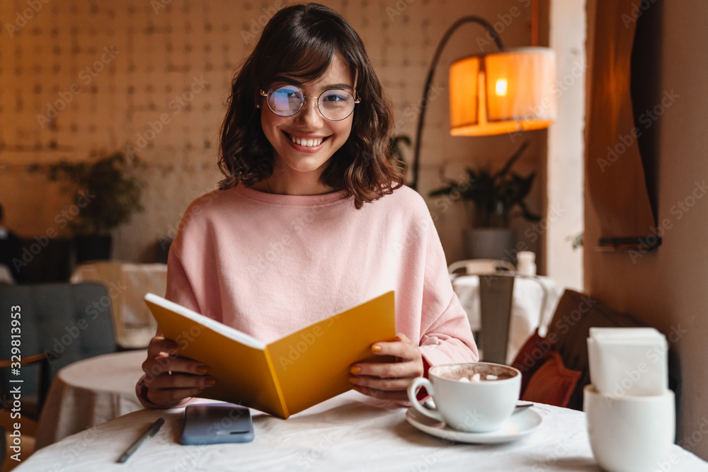 Brunette young woman indoors in cafe reading book. Brunette young woman indoors in cafe reading book.
