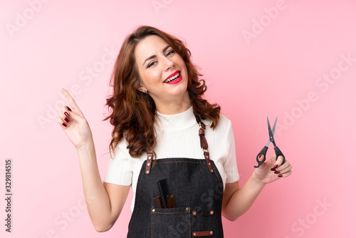 Young Russian woman over isolated pink background with hairdresser or barber dress and pointing side