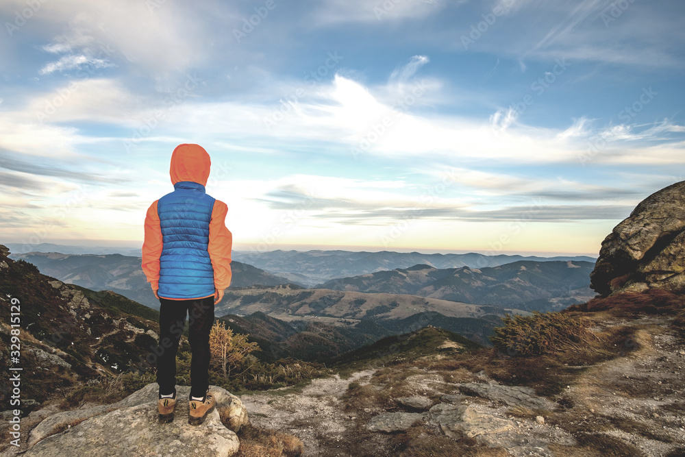 Young child boy hiker standing in mountains enjoying view of amazing mountain landscape.