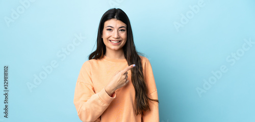 Young brunette girl over isolated blue background pointing to the side to present a product