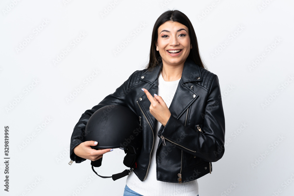 Young woman holding a motorcycle helmet over isolated white background pointing finger to the side Young woman holding a motorcycle helmet over isolated white background pointing finger to the side