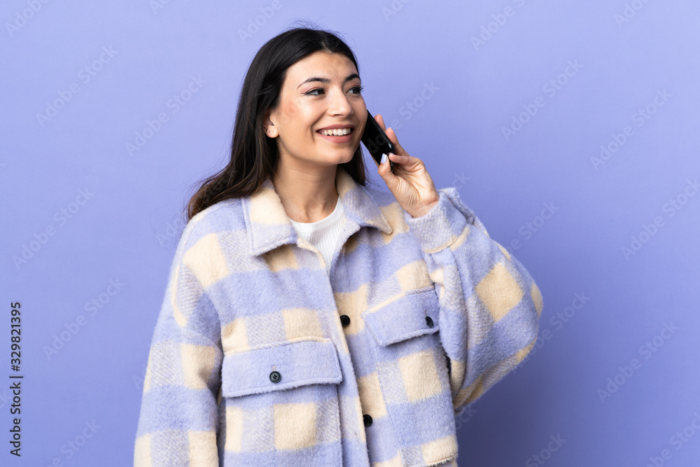Young brunette woman over isolated purple background keeping a conversation with the mobile phone Young brunette woman over isolated purple background keeping a conversation with the mobile phone