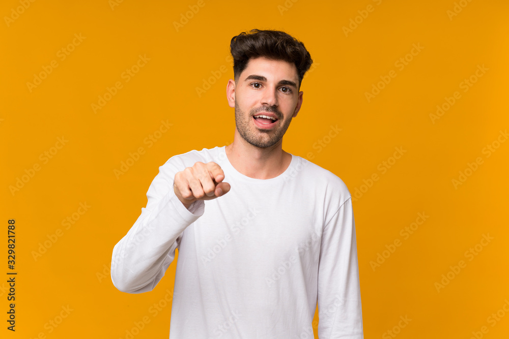 Young man over isolated orange background surprised and pointing front Young man over isolated orange background surprised and pointing front