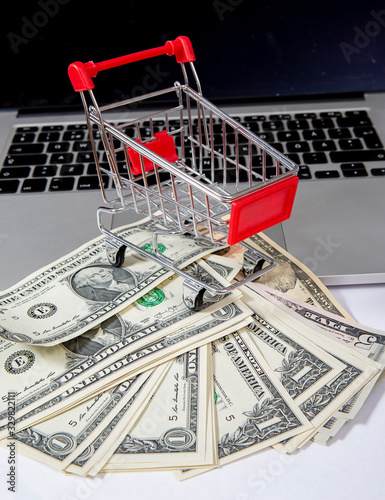 Online shopping concept image with miniature shopping cart and cash on a laptop.