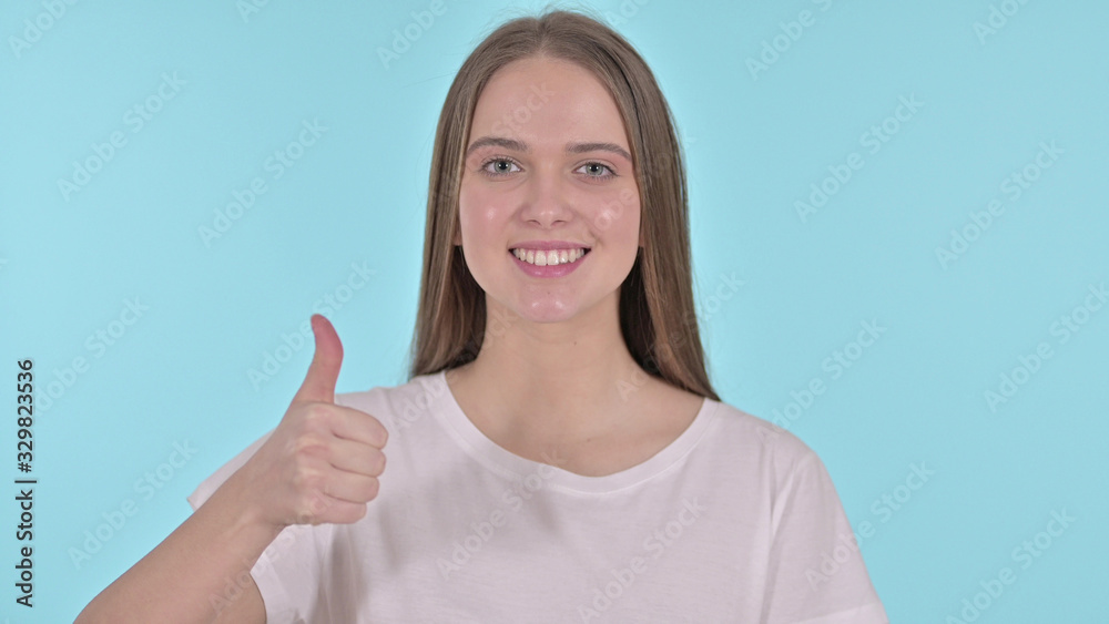Thumbs Up by Cheerful Beautiful Young Woman, Blue Background Thumbs Up by Cheerful Beautiful Young Woman, Blue Background