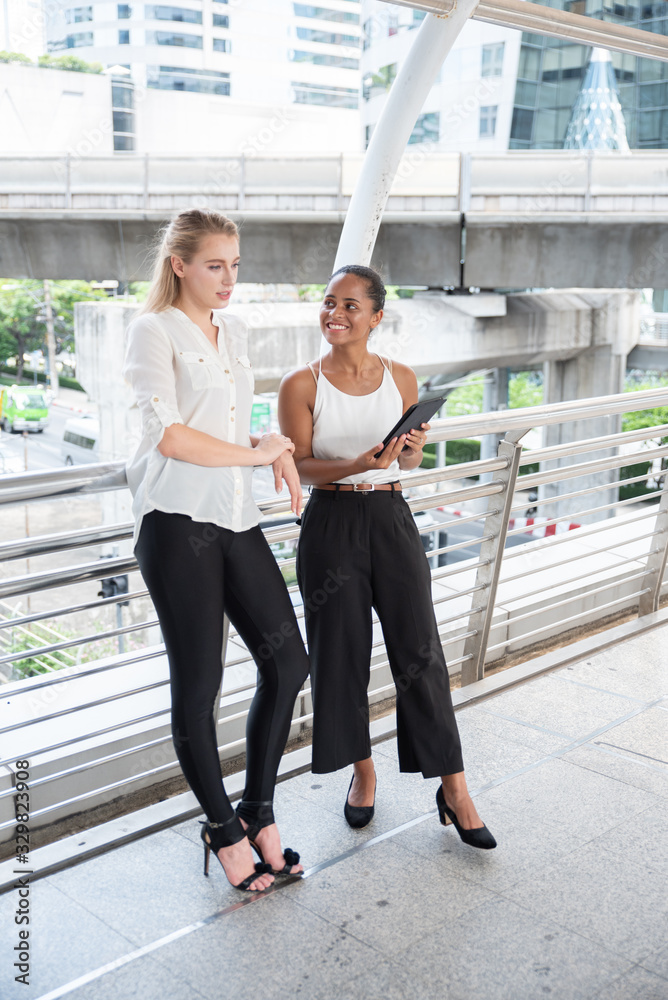 Obraz premium Businesswoman Showing Digital Tablet To Female Colleague On Walkway Bridge In City