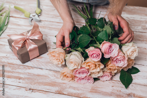 Hands of young woman florist working with fresh flowers making bouquet of pink roses on table. © Ira_Shpiller