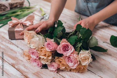 Hands of young woman florist working with fresh flowers making bouquet of pink roses on table.