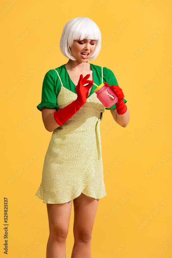 emotional pop art woman in yellow dress and white wig looking with disgust on drink in jar, isolated on yellow emotional pop art woman in yellow dress and white wig looking with disgust on drink in jar, isolated on yellow