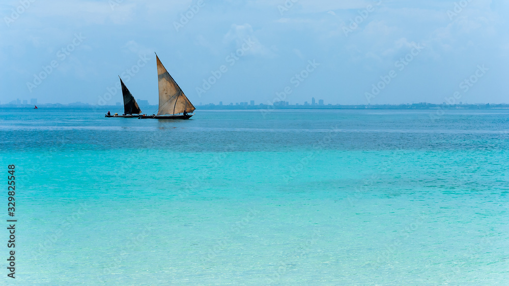 Obraz premium Traditional dhow sails boat on Azure blue waters with an urban skyline in the distance on sea scapes