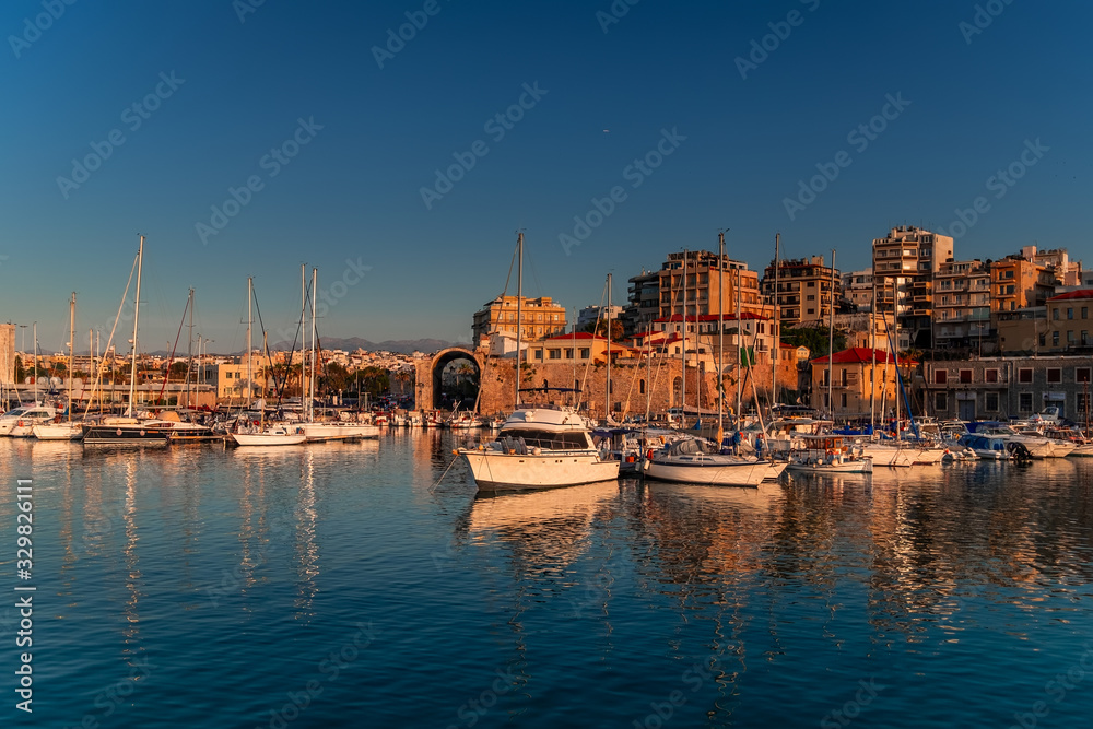 Panoramic view of beautiful sunset in Koules Fortress (Rocca a Mare), Crete island. Yachts reflecting in the mirror of water near Venetian old harbor in Heraklion city. Amazing destination in Greece