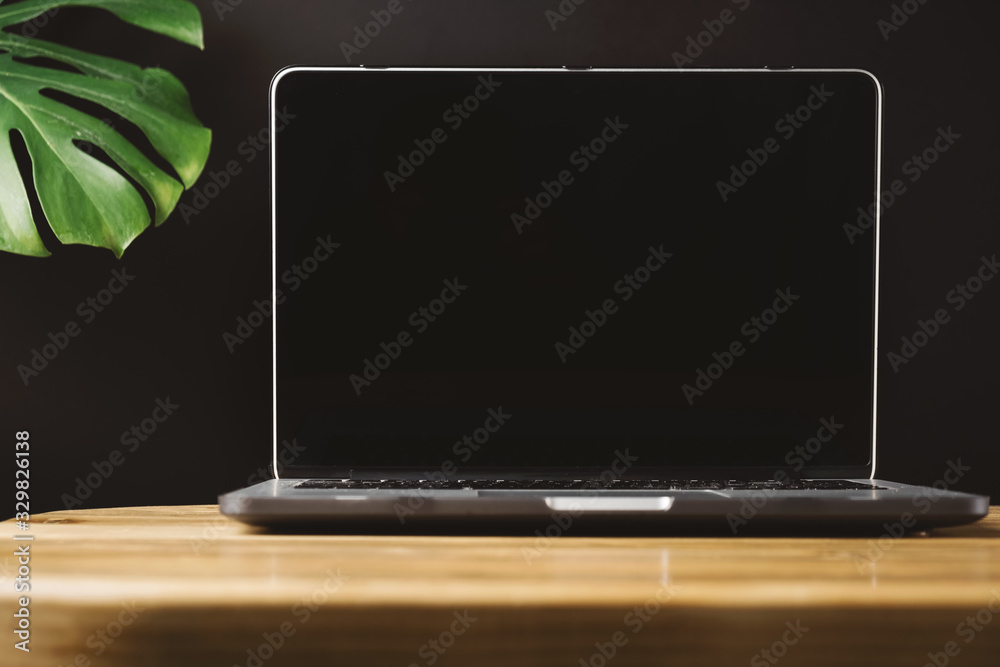 Blank screen laptop on wooden table with exotic tropical leaf monstera on grey background in minimal style. Front view social media, website, blog hero header template. Blank screen laptop on wooden table with exotic tropical leaf monstera on grey background in minimal style. Front view social media, website, blog hero header template.