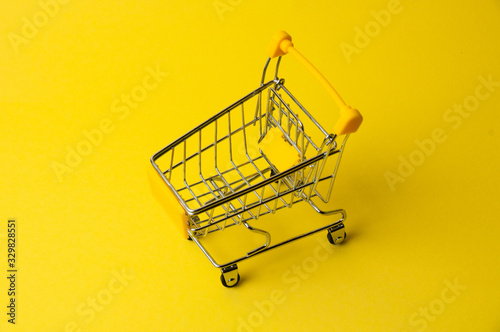 Cart for shopping on a yellow background. Supermarket food price concept, holiday discounts