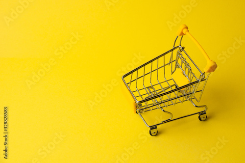 Cart for shopping on a yellow background. Supermarket food price concept, holiday discounts