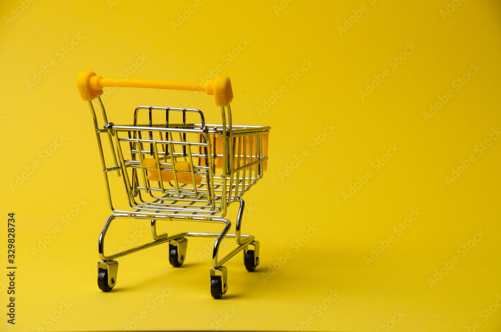 Cart for shopping on a yellow background. Supermarket food price concept, holiday discounts Cart for shopping on a yellow background. Supermarket food price concept, holiday discounts