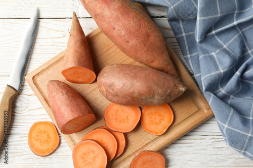 Sweet potato, knife, board and towel on wooden background, top view