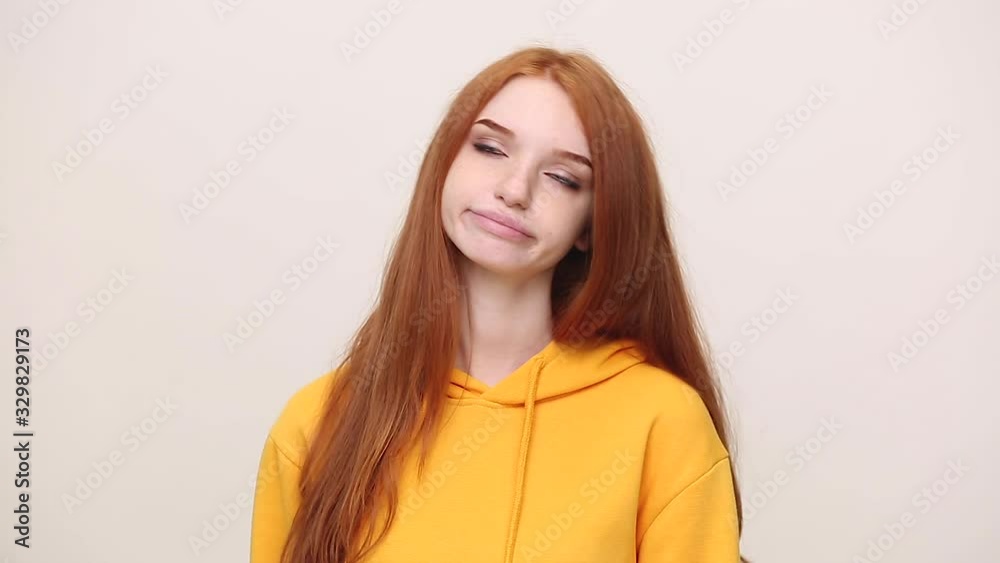 Boring ginger redhead curly young girl in yellow streetwear hoodie posing isolated on white background in studio. People lifestyle concept. Looks around bites her lips misses and waiting for something Boring ginger redhead curly young girl in yellow streetwear hoodie posing isolated on white background in studio. People lifestyle concept. Looks around bites her lips misses and waiting for something