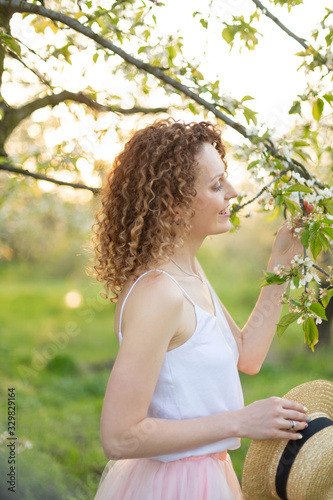 Young attractive woman with curly hair walking in a green flowered garden. Spring mood photo