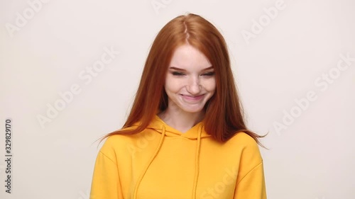 Pretty ginger curly young girl in yellow streetwear hoodie posing isolated on white background in studio. People sincere emotions lifestyle concept. Looking at camera approvingly at camera nod head