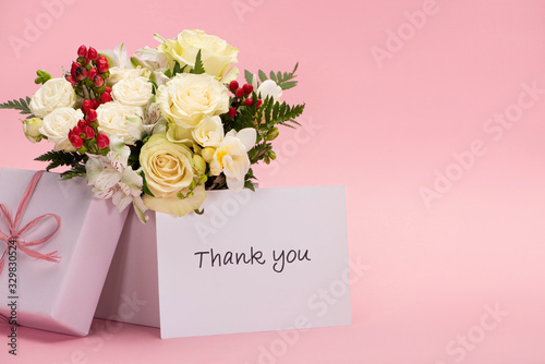bouquet of flowers in festive gift box with bow near thank you card on pink background