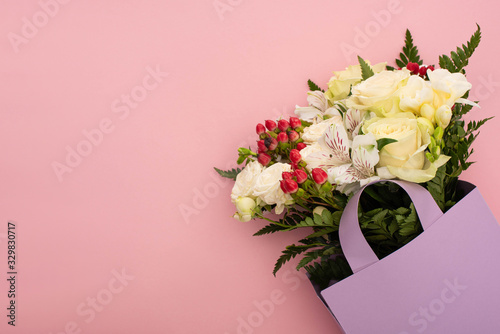 top view of bouquet of flowers in violet paper bag on pink background