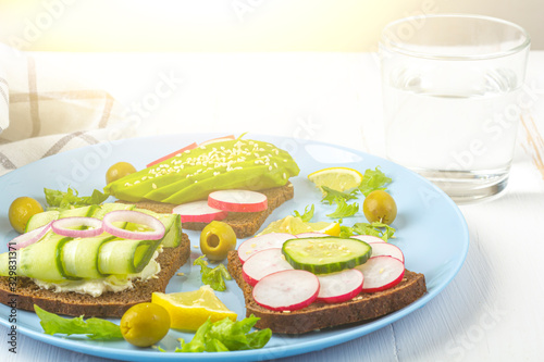 Superfood open vegetarian sandwich with different toppings  avocado  cucumber  radish on plate and glass of water on white background. Healthy eating. Organic and veggie food. Copy space for text