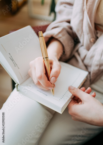 A thoughtful serious girl blogger freelancer works at home on a laptop, writes ideas in her notebook diary, and organizes in a bright spacious office with a view of the city decorated with greenery