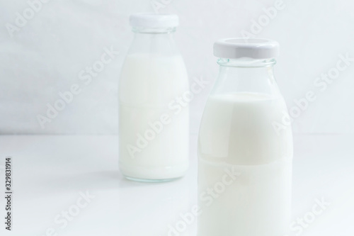 Two glass bottle of milk on the white table on a blue background for food healthy concept with copy space for text.