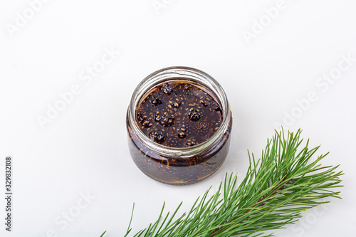 Unusual jam from pine cones in glass jar on white background among pine branches and cones. Organic and vegetarian sweet dessert close up, copy space for text. Remedy for colds