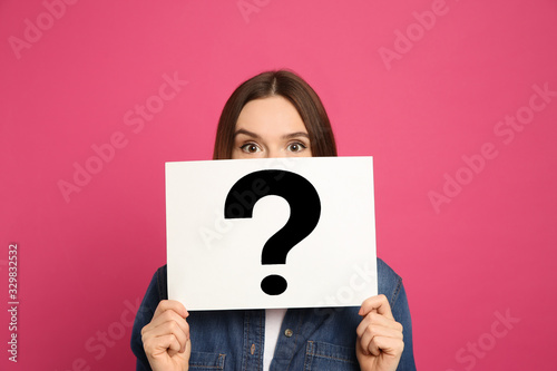 Emotional woman holding question mark sign on pink background photo