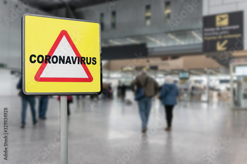 Warning sign with text Coronavirus on a generic airport with passengers walking towards the boarding gates. Coronavirus crisis concept